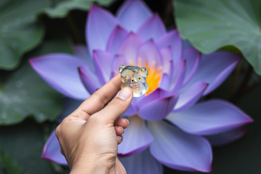 Hand holding a clear gummy shaped like an animal face in front of a blooming purple lotus flower