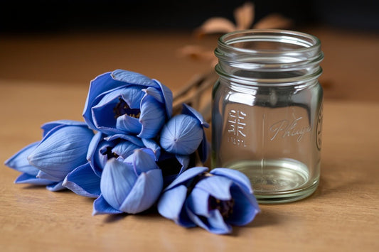 Close-up of blue lotus flowers next to an empty glass jar on a wooden surface