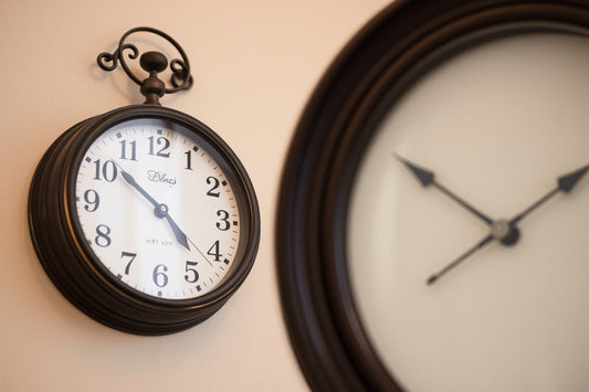 Vintage black wall clock showing 4:52 with blurred larger clock in background